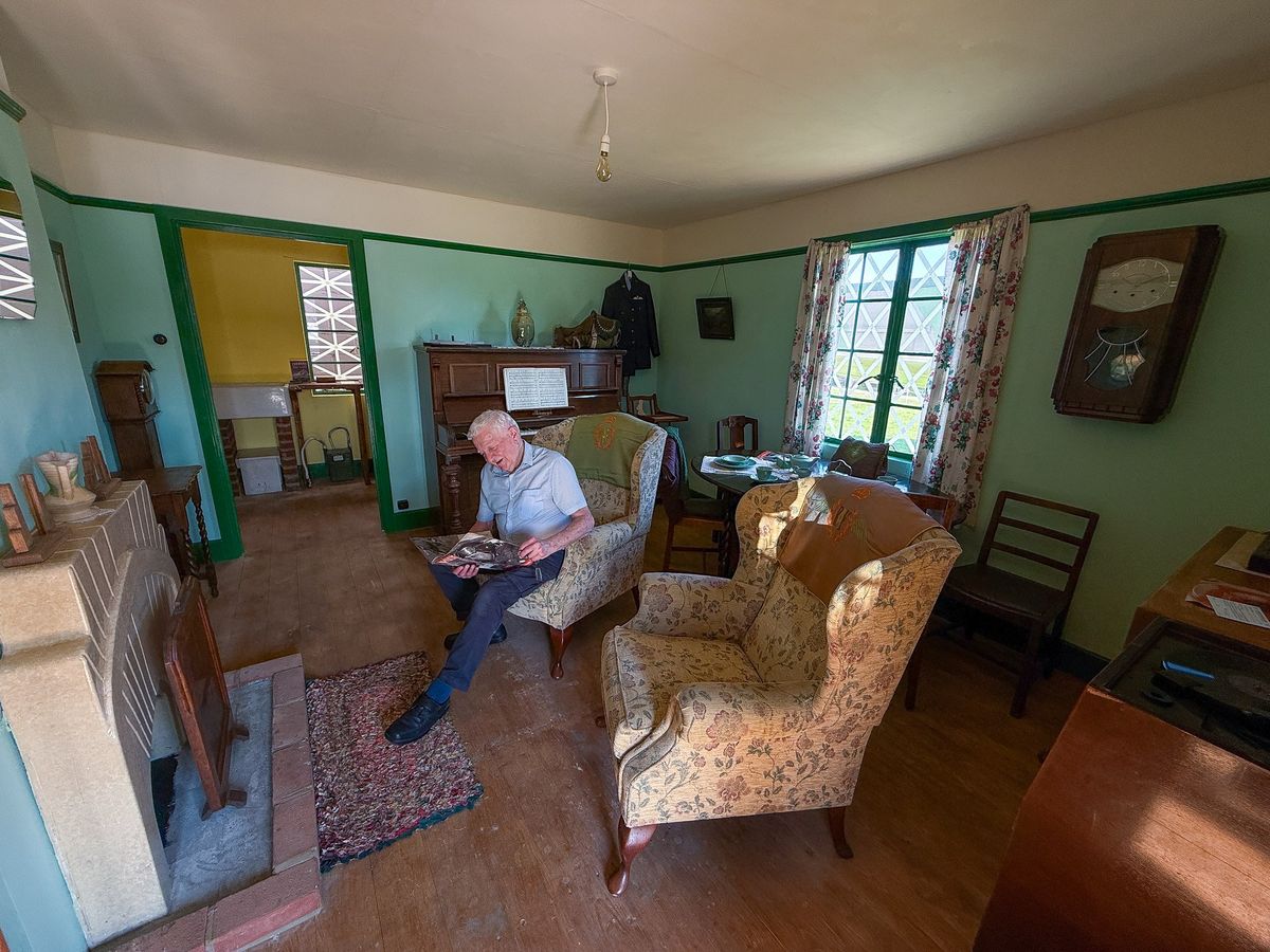 A visitor reading in an armchair in the recreated 1940s sitting room, with the piano against the far wall