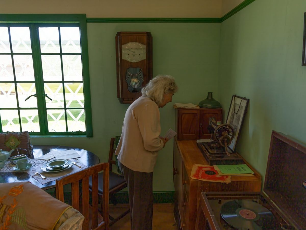 A visitor looking at the wall clock and period memorabilia in the recreated wartime room, with a gramophone and tea table